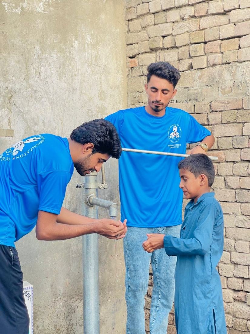 DPO volunteers helping a child drink clean water from a new pump